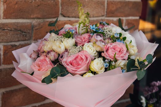 A vibrant bouquet of flowers with pink roses and greenery against a brick backdrop.