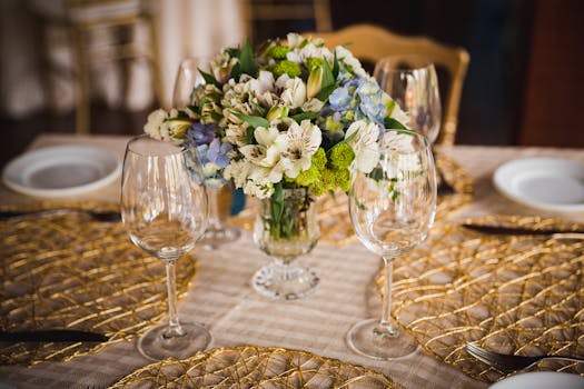 Elegant floral arrangement on a table with wine glasses and golden placemats, perfect for events.